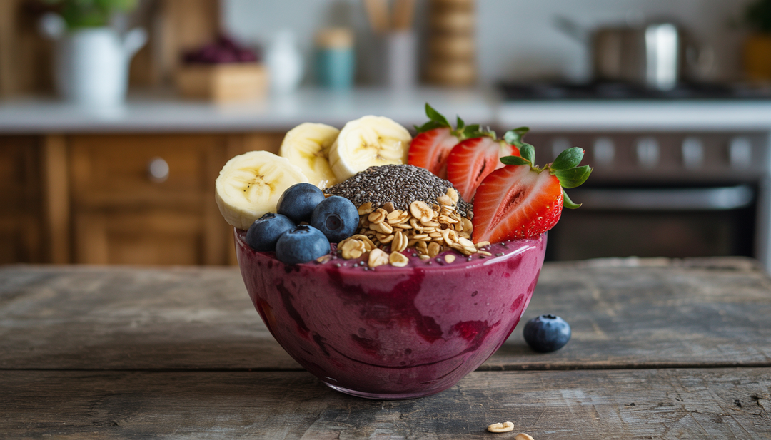 A colorful acai bowl with banana slices, strawberries, blueberries, granola, and chia seeds on a wooden table, set against a blurred kitchen background.
