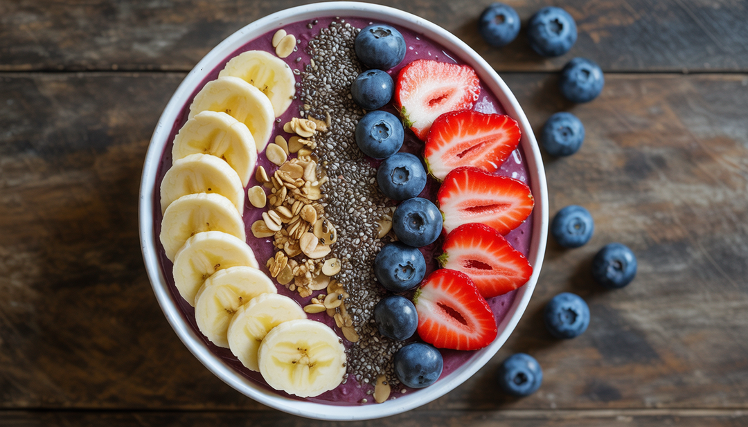 A colorful acai bowl topped with bananas, strawberries, blueberries, chia seeds, and granola on a wooden table.