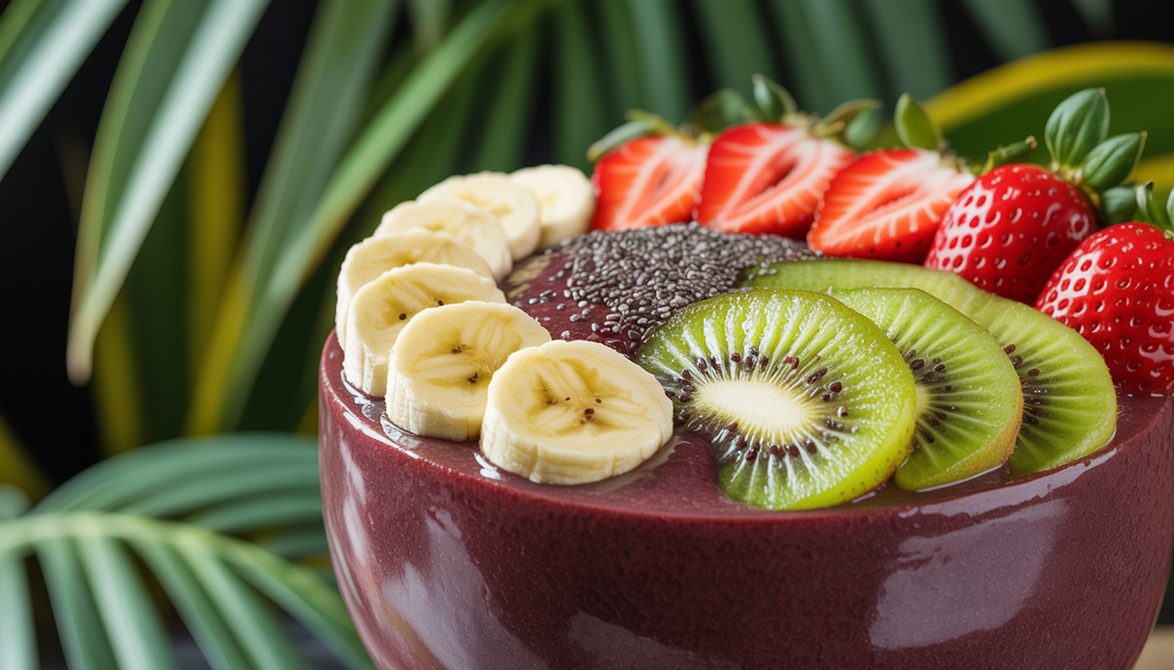 A close-up of an acai bowl with a dark purple base, topped with banana, strawberry, and kiwi slices, and chia seeds, set against a tropical backdrop with lush greenery.