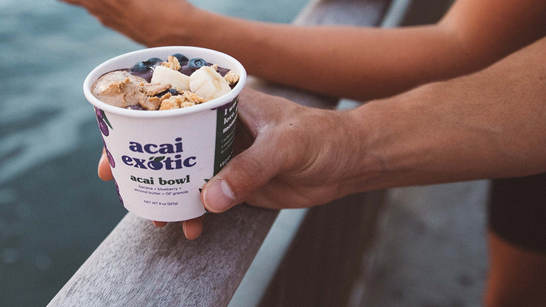 Hands holding an Acai Exotic acai bowl cup by the water