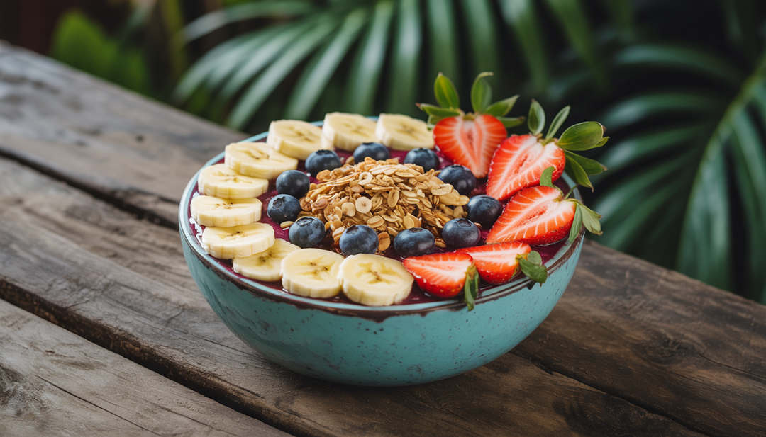 A colorful acai bowl topped with bananas, strawberries, blueberries, and granola on a wooden table with a tropical background.
